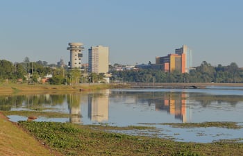 Paisaje urbano junto a un cuerpo de agua, con edificios altos y vegetación en los bordes, sin personas visibles.