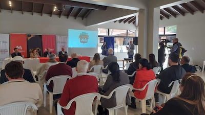 Panel de cuatro personas, incluyendo a una mujer hablando, con un proyector visiblemente iluminado en un ambiente moderno.