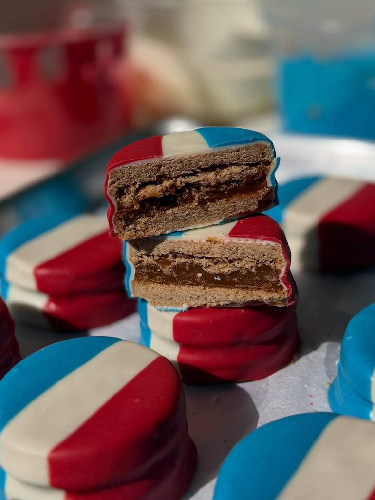 Galletas decoradas en rojo y azul, una galleta cortada revela su relleno de caramelo, dispuestas en una superficie de cocina.