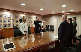 Hombre en traje jurando con la mano levantada, rodeado de hombres en trajes oscuros y un representante indígena con tocado.