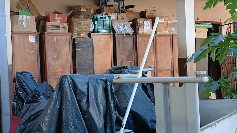 Almacén desorganizado de la Escuela Inmaculada Concepción, con objetos apilados y plásticos negros cubriendo partes del entorno.