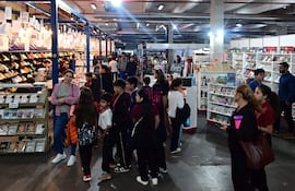 Jóvenes sonrientes exploran estantes llenos de libros en un ambiente iluminado de la Feria Internacional del Libro.