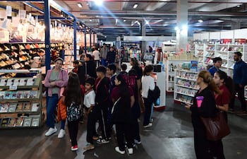 Jóvenes sonrientes exploran estantes llenos de libros en un ambiente iluminado de la Feria Internacional del Libro.