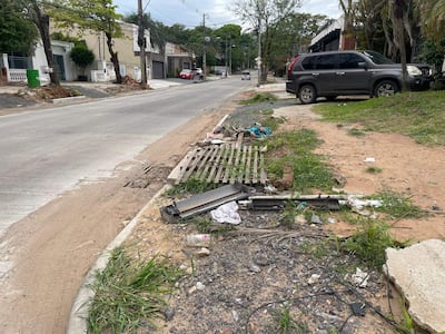 Vereda y calzada en obras, SUV gris estacionado, restos de escombros y basura en un entorno urbano despejado.
