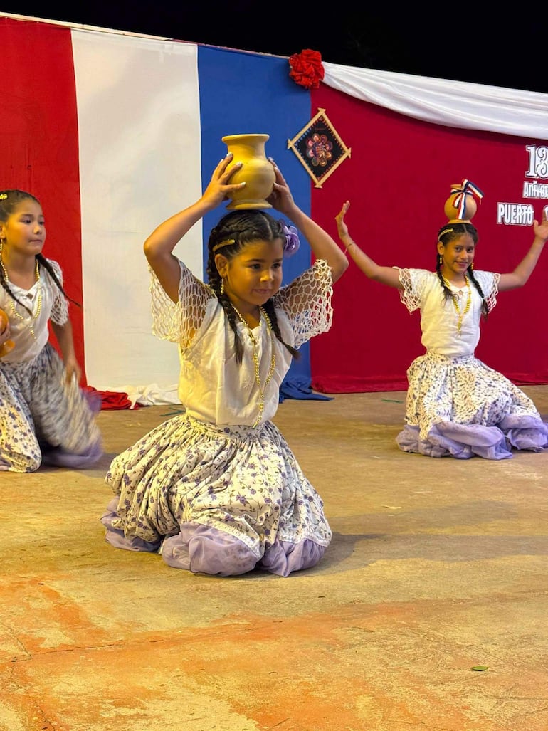 Niñas bailando en trajes tradicionales con blusas blancas y faldas florales, decoradas con colores de la bandera paraguaya.