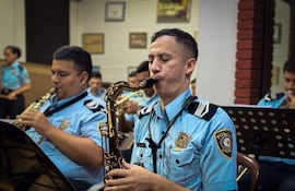 Cuatro músicos de la Policía Nacional en uniforme azul celeste tocan saxofones durante un ensayo en un auditorio.