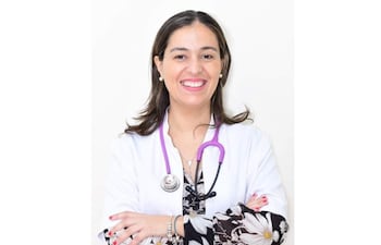 Dra. Irene Benítez sonriente, con bata blanca y estetoscopio púrpura, en fondo blanco.