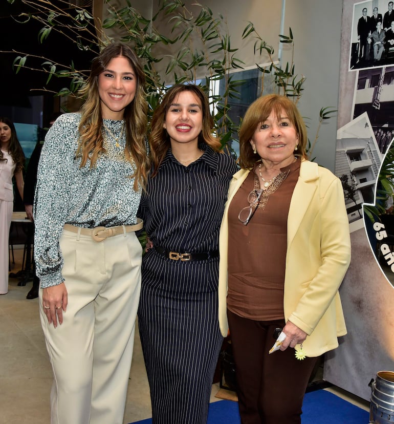 Tres mujeres sonríen en un ambiente decorado, una usa chaqueta amarilla, otra blusa de flores y la tercera camisa a rayas.