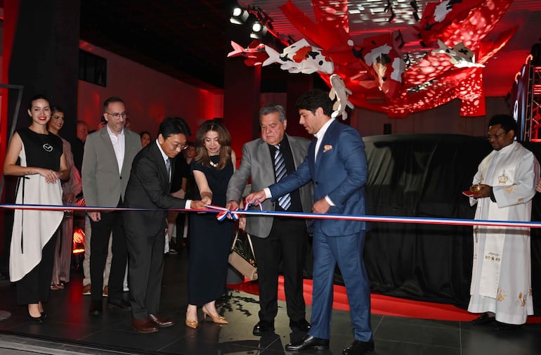 Ñufro Arias y Didier Arias en la ceremonia de inauguración, luciendo trajes elegantes y rodeados de luces rojas en un ambiente festivo.