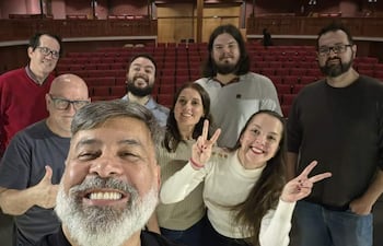 Hombre con barba sonriente y cinco personas más en el teatro, todos lucen felices tras el evento. Asientos rojos de fondo.