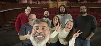 Hombre con barba sonriente y cinco personas más en el teatro, todos lucen felices tras el evento. Asientos rojos de fondo.