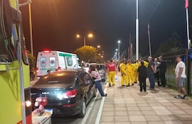 Rescatistas de traje amarillo atienden el accidente en la avenida, con dos ambulancias visibles en el fondo.