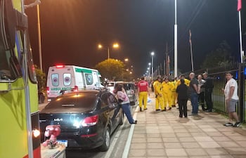 Rescatistas de traje amarillo atienden el accidente en la avenida, con dos ambulancias visibles en el fondo.