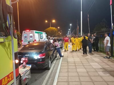 Rescatistas de traje amarillo atienden el accidente en la avenida, con dos ambulancias visibles en el fondo.