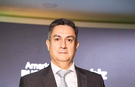 Carson Villalba en traje oscuro y corbata, de pie con expresión seria en un ambiente iluminado con fondo elegante.