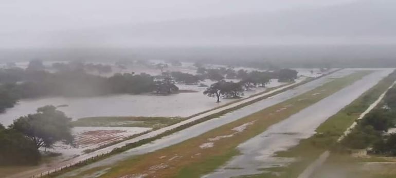 Paisaje inundado por lluvias intensas, con árboles dispersos y cielo grisáceo, sin personas visibles.