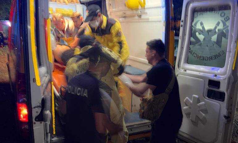 Cinco personas, cuatro con uniformes de urgencia y uno de policía, ayudan a un herido sobre una camilla en un ambiente nocturno.