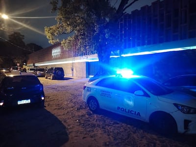 Escena nocturna con vehículo policial azul iluminando la calle, sin personas visibles alrededor.