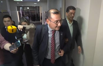 Miguel Mora, con corbata roja y camisa clara, se retira mientras una mujer lo entrevista, con un fondo de asistentes.