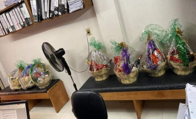 Cestas decoradas en papel celofán sobre un banco negro, rodeadas de documentos y un ventilador en un ambiente de oficina.