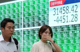 Peatones pasan junto a un cartel que exhibe información sobre el nikkei en la bolsa de valores, con su mayor pérdida de la historia en Tokio, Japón.
