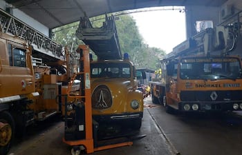 Taller con camiones de bomberos, uno amarillo y otro marrón, en ambiente iluminado con herramientas de mantenimiento visibles.