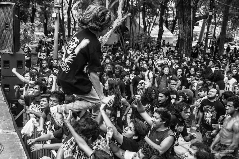 Jóvenes con camisetas de bandas de metal disfrutan en un concierto al aire libre, algunos levantando los puños en señal de entusiasmo.