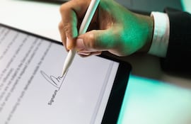 Primer plano de la mano de un empresario firmando electrónicamente en una tableta con un lápiz óptico.