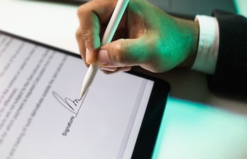 Primer plano de la mano de un empresario firmando electrónicamente en una tableta con un lápiz óptico.