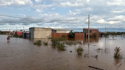 Hombre agachado en agua, sostiene un palo, rodeado de edificios con solo partes superiores visibles y cielo nublado.