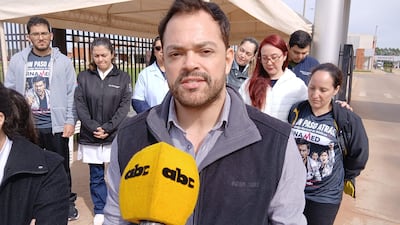 Hombres y mujeres en protesta frente a un hospital, algunos con camisetas que dicen 'UN PASO ATRÁS', expresiones serias.