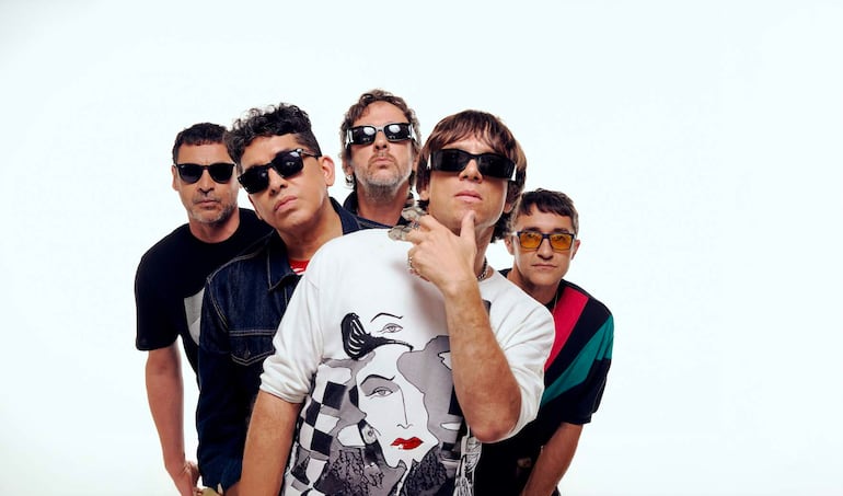 Cinco hombres con gafas oscuras posan en un estudio, mostrando diversas expresiones y estilos de ropa.