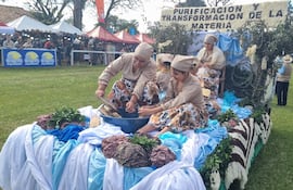 Cinco mujeres en atuendos tradicionales trabajan en un bol grande, rodeadas de telas de colores y un cartel sobre transformación de materia.