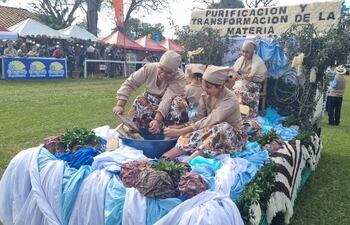 Cinco mujeres en atuendos tradicionales trabajan en un bol grande, rodeadas de telas de colores y un cartel sobre transformación de materia.