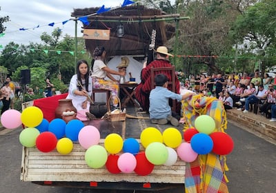 Cinco participantes del desfile en ropa tradicional con globos de colores y una audiencia de fondo, celebrando la primavera.
