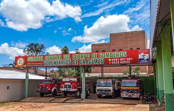 Cartel del Cuartel de Bomberos de Caaguazú con vehículos de emergencias rojos y blancos estacionados bajo un cielo despejado.