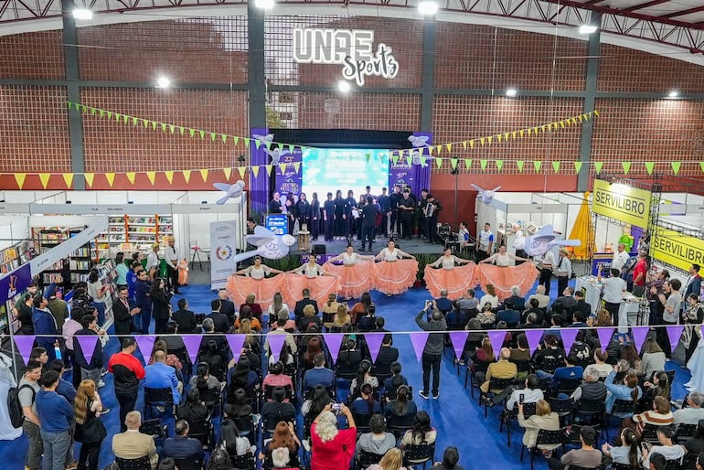 Artistas en escenario con vestimentas brillantes, mientras la audiencia observa atentamente el evento cultural.