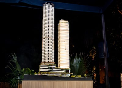 Modelo arquitectónico de dos torres iluminadas, con base negra y plantas decorativas alrededor en un entorno cuidado.