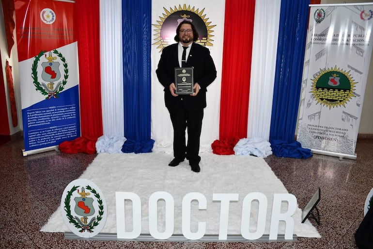 El concejal Jaime Rolando Méndez sostiene su título de doctor en una ceremonia del Instituto de Altos Estudios Estratégicos.