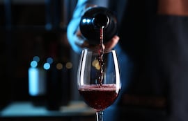 Mano vertiendo vino tinto de una botella a una copa en un ambiente acogedor y elegante.