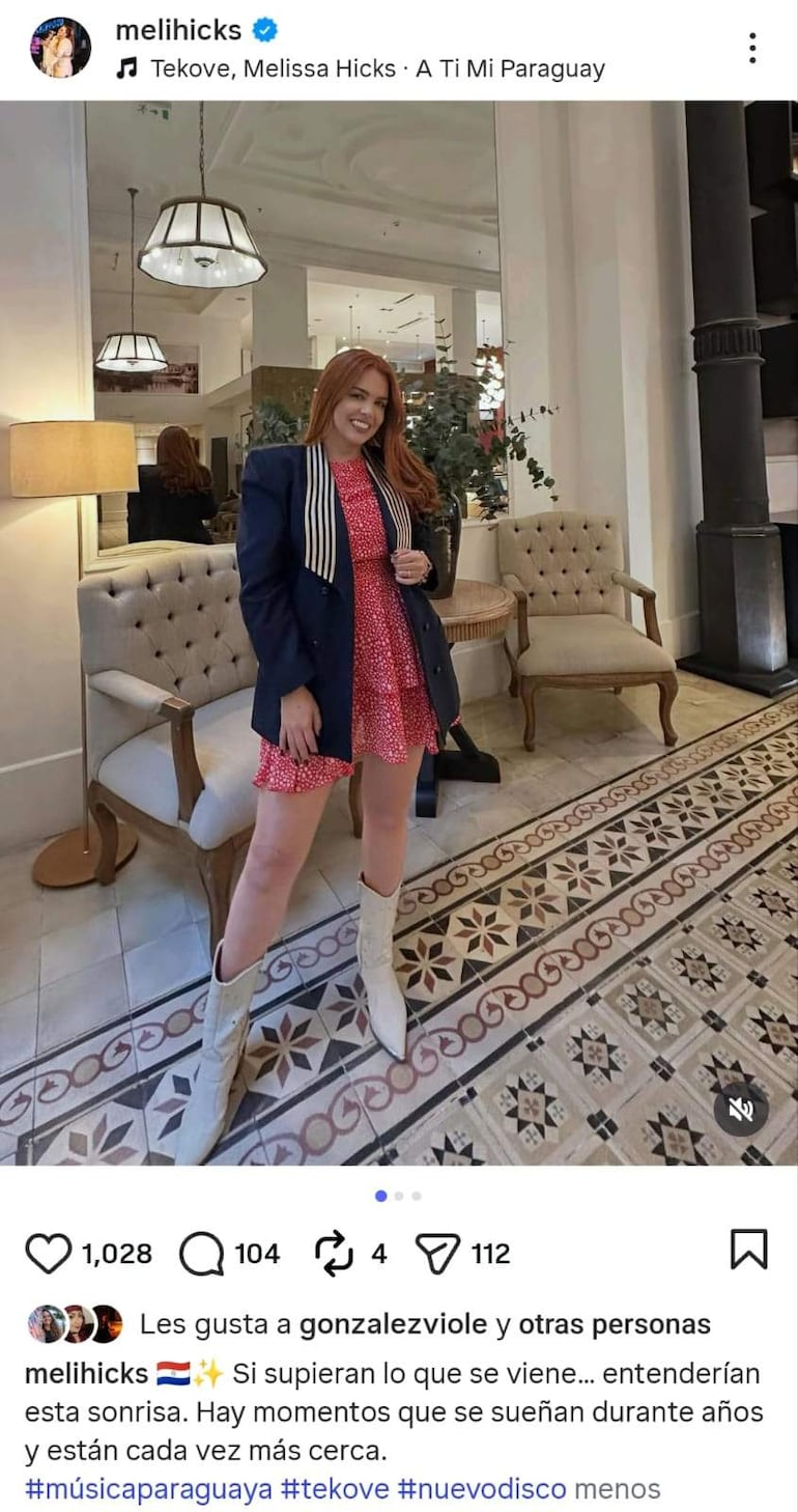 Melissa Hicks con sonrisa confiada, lleva un vestido rojo con puntos blancos y chaqueta oscura, posando en un entorno elegante.