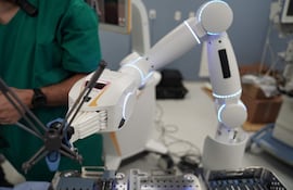 Brazo robótico en un entorno médico iluminado, con mano en camisa verde interactuando con dispositivo.