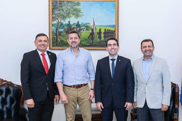 Pedro Alliana en blazer oscuro, Marcelo Soto en camisa clara, todos sonrientes en una oficina con cuadro histórico.