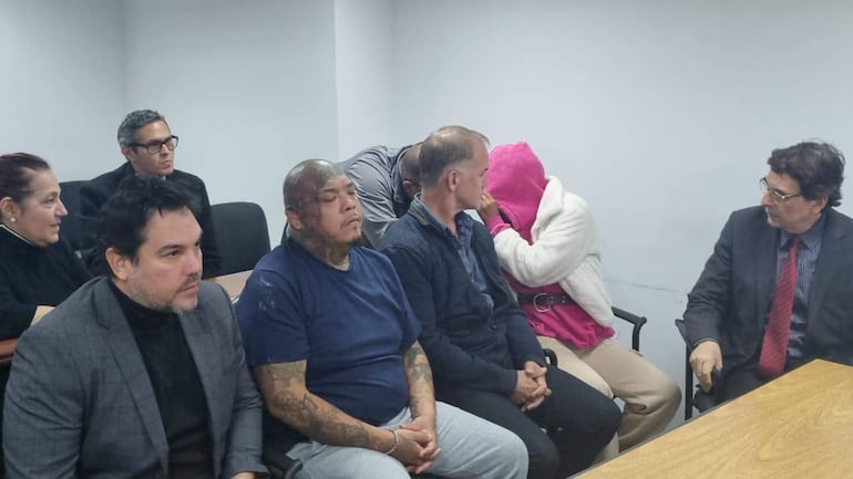 Óscar Tuma y Rafael Fernández junto a tres imputados en audiencia, expresiones serias y ambiente austero.