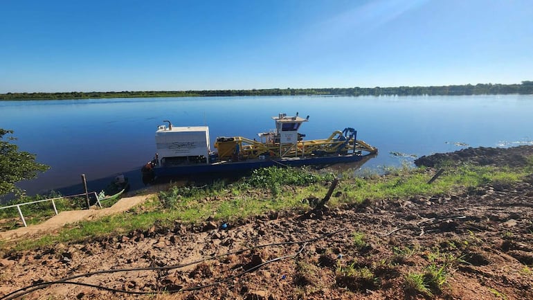 Barco de mantenimiento en el río Paraguay, con estructura blanca y azul, bajo un cielo despejado y vegetación alrededor.