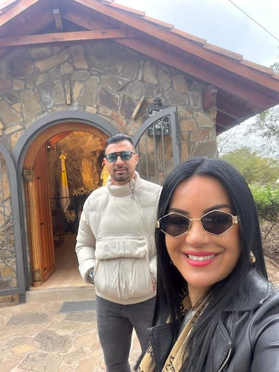 Julio César Cáceres con chaqueta blanca y gafas de sol, junto a Gloria Vera en chaqueta negra, ambos sonriendo en un entorno rústico.