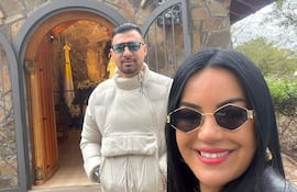 Julio César Cáceres con chaqueta blanca y gafas de sol, junto a Gloria Vera en chaqueta negra, ambos sonriendo en un entorno rústico.