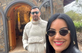 Julio César Cáceres con chaqueta blanca y gafas de sol, junto a Gloria Vera en chaqueta negra, ambos sonriendo en un entorno rústico.