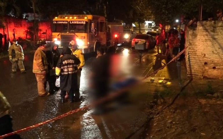 Uniformados de la Policía Nacional evalúan la situación, con un camión de bomberos iluminando la escena en una calle mojada.
