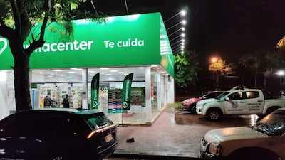 Fachada de la farmacia FarmaCenter iluminada y vehículos estacionados, con una camioneta de la Policía Nacional a la vista.
